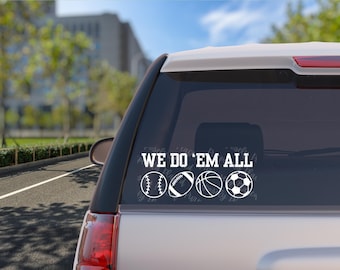 May include: White vinyl decal with the text "We Do 'Em All" and five different sports ball icons: baseball, football, basketball, soccer ball, and volleyball. The decal is on the back window of a silver SUV.