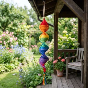 May include: A hanging spiral ornament crafted from crocheted yarn in a vibrant rainbow gradient, transitioning from red at the top to orange, yellow, green, blue, and purple at the bottom, finished with a small wooden bead and a colorful tassel.