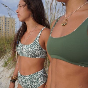 May include: Two women wearing green and white patterned bikini tops and bottoms. One bikini top is solid green and the other has a floral pattern. Both women are wearing gold jewellery.