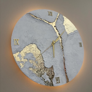 May include: A white circular clock with gold Roman numeral markings and gold accents. The clock face has a textured, cracked appearance with gold leaf accents.