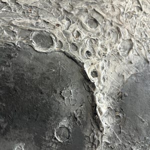 Peut inclure: Gros plan sur une surface textur&eacute;e, grise et noire, avec une texture rugueuse et irr&eacute;guli&egrave;re. La surface pr&eacute;sente une vari&eacute;t&eacute; de crat&egrave;res et d'indentations, ressemblant &agrave; la surface de la lune.