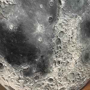 Peut inclure: Gros plan d'une sculpture ronde de lune textur&eacute;e en gris et blanc. La surface de la lune est textur&eacute;e pour ressembler aux crat&egrave;res et &agrave; la surface de la lune.