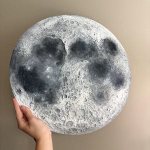 Peut inclure: Une lune peinte en blanc et gris avec une surface textur&eacute;e, ressemblant &agrave; la surface de la vraie lune.