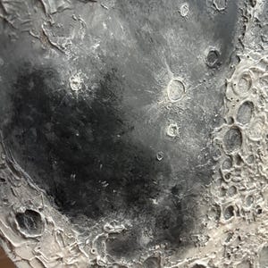 Peut inclure: Gros plan sur une surface textur&eacute;e grise et blanche ressemblant &agrave; la surface de la lune. La surface pr&eacute;sente des crat&egrave;res et une texture rugueuse et irr&eacute;guli&egrave;re.