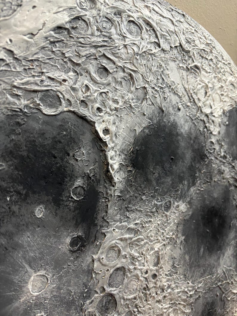 Peut inclure: Gros plan sur une peinture de lune textur&eacute;e, grise et blanche. La surface de la lune est peinte avec une vari&eacute;t&eacute; de textures, y compris des crat&egrave;res et des cr&ecirc;tes.