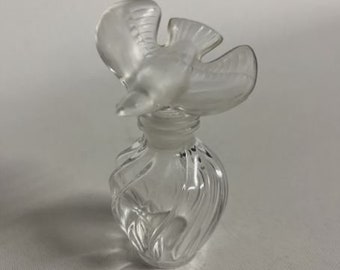 Può includere: Un flacone di vetro trasparente con un tappo di vetro smerigliato a forma di uccello. Il flacone ha un design testurizzato e rigato.