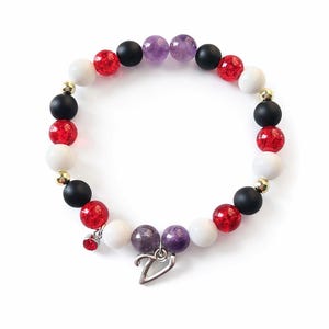 May include: A beaded bracelet featuring a mix of red, white, black, and purple beads. The bracelet includes a silver heart charm and a small red charm. The beads are interspersed with gold-colored spacers.