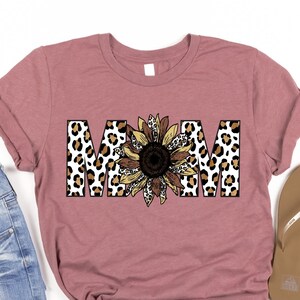May include: A mauve t-shirt with the word "MOM" in brown, black, and white leopard print letters with a sunflower in the center.