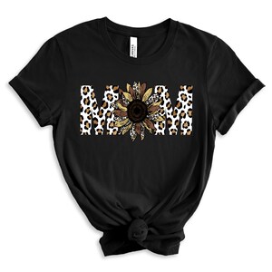 May include: Black t-shirt with the word "MOM" in white letters with a leopard print and sunflower design.