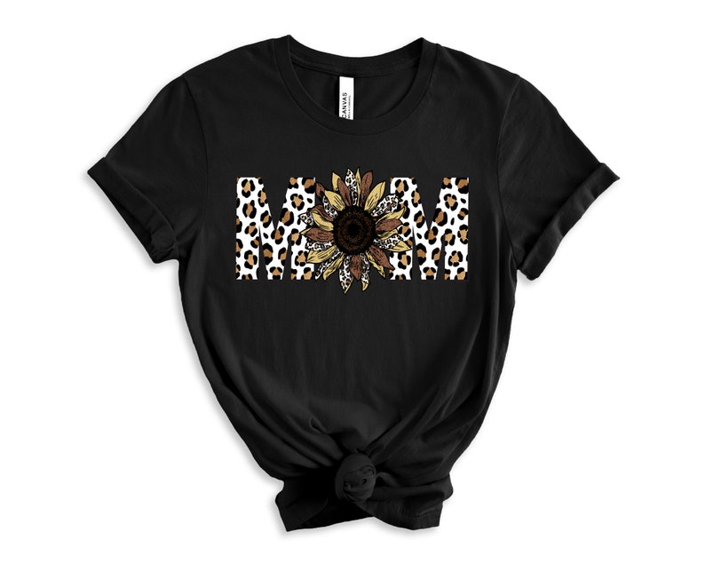 May include: Black t-shirt with the word "MOM" in white letters with a leopard print and sunflower design.