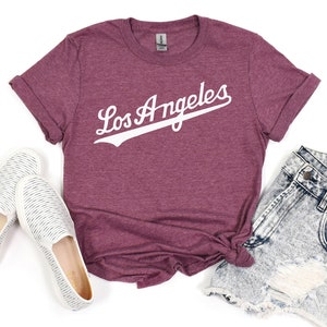 May include: A maroon t-shirt with the text "Los Angeles" in white with a baseball-style font and a white baseball-style line under the text.