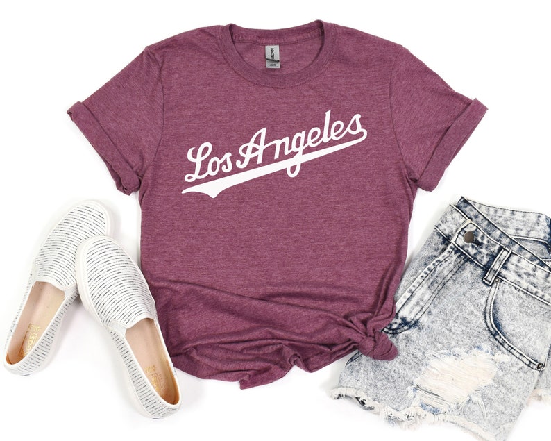 May include: A maroon t-shirt with the text "Los Angeles" in white with a baseball-style font and a white baseball-style line under the text.