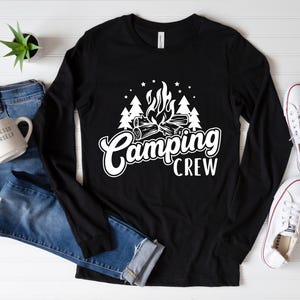 Pode incluir: Camiseta preta de manga comprida com um gr&aacute;fico branco de uma fogueira e &aacute;rvores. O texto "Camping Crew" &eacute; impresso abaixo do gr&aacute;fico.