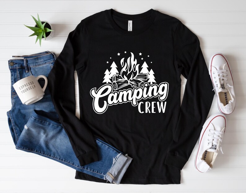 Pode incluir: Camiseta preta de manga comprida com um gr&aacute;fico branco de uma fogueira e &aacute;rvores. O texto "Camping Crew" &eacute; impresso abaixo do gr&aacute;fico.