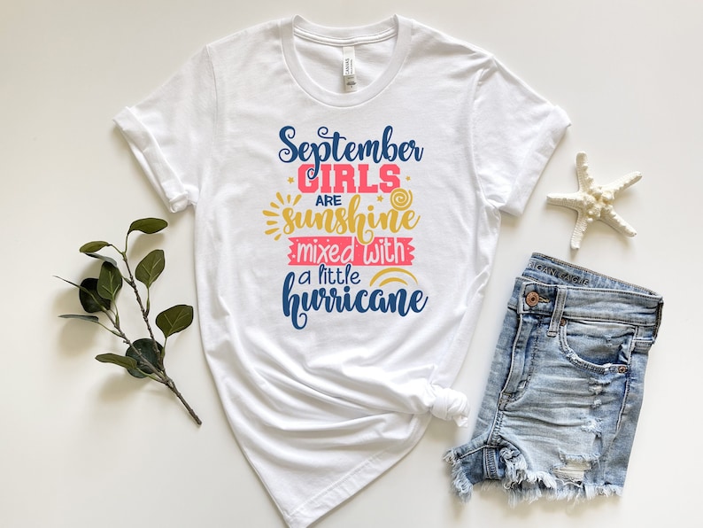 May include: White t-shirt with a blue and pink graphic that says "September girls are sunshine mixed with a little hurricane".