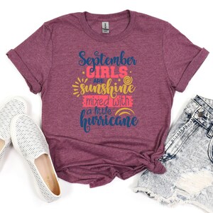 May include: A maroon t-shirt with the text "September girls are sunshine mixed with a little hurricane" in navy blue and pink lettering.