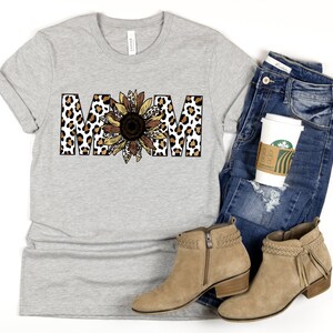 May include: A gray t-shirt with the word "MOM" printed in brown and black leopard print with a sunflower in the center.