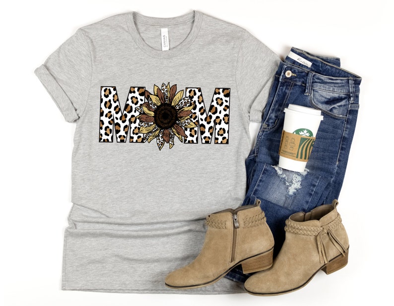 May include: A gray t-shirt with the word "MOM" printed in brown and black leopard print with a sunflower in the center.