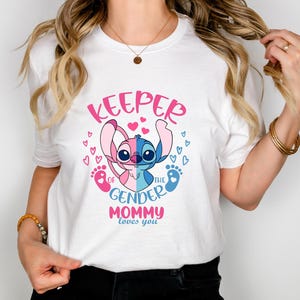 May include: White t-shirt with a pink and blue Stitch character holding a pink and blue baby foot print. The text on the shirt reads "Keeper of the Gender Mommy loves you".