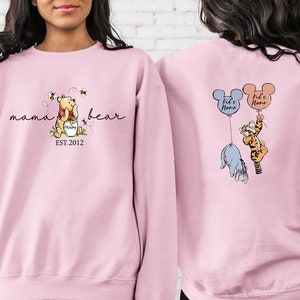 Pu&ograve; includere: Una felpa rosa chiaro con Winnie the Pooh, il testo "mama bear" e "EST. 2012" sul davanti. Il retro della felpa mostra Eeyore e Tigro che tengono in mano dei palloncini con la scritta "Kid's Name".