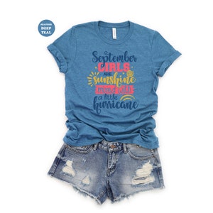 May include: A heather deep teal t-shirt with the text "September girls are sunshine mixed with a little hurricane" in a colorful font.