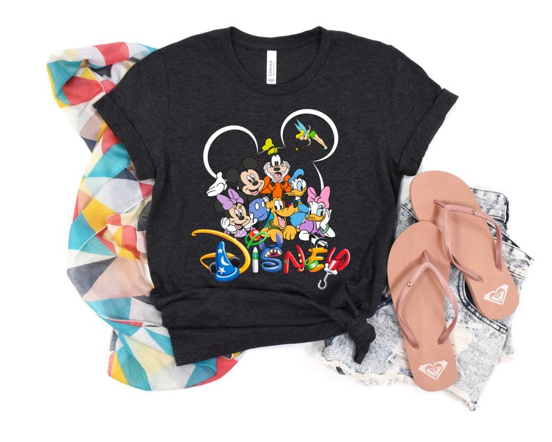 May include: Dark gray t-shirt featuring a colorful Disney character graphic. The graphic includes Mickey Mouse, Minnie Mouse, Donald Duck, and other characters. Pink flip-flops and a patterned scarf are also in the image.