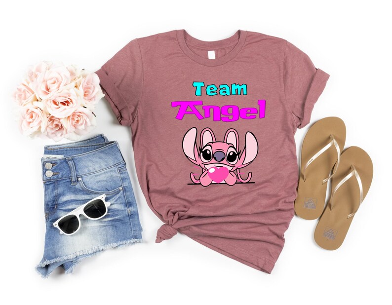 May include: A pink heather t-shirt with the text "Team Angel" in blue and pink lettering. A pink Stitch character with a heart is below the text.