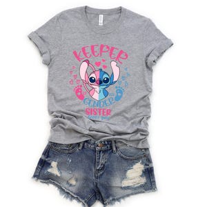 May include: Gray t-shirt with a pink and blue Stitch character and the text "Keeper of my gender sister loves you".