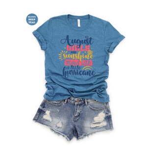 May include: A heather deep teal t-shirt with the text "August girls are sunshine mixed with a little hurricane" in pink, yellow, and blue lettering.