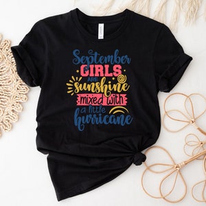 May include: Black t-shirt with the text "September Girls are sunshine mixed with a little hurricane" in colorful lettering.