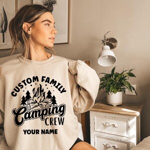 Pode incluir: Uma camisa de moletom bege com um design gr&aacute;fico preto que diz "Custom Family Camping Crew" e "Your Name".