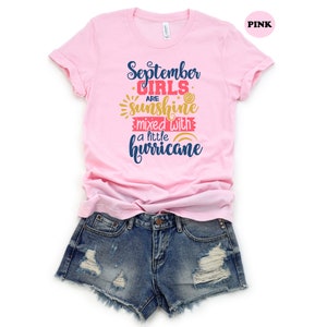 May include: Pink t-shirt with the text "September girls are sunshine mixed with a little hurricane" in blue, yellow, and red lettering.