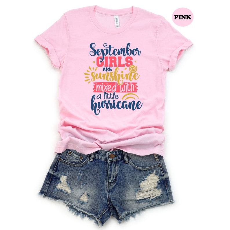 May include: Pink t-shirt with the text "September girls are sunshine mixed with a little hurricane" in blue, yellow, and red lettering.