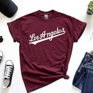 May include: A maroon t-shirt with a white graphic that says "Los Angeles" in a vintage baseball font.