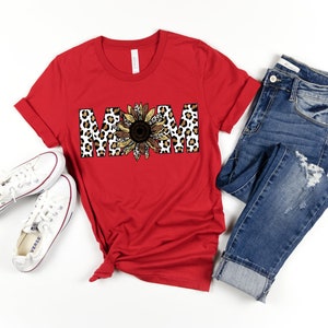 May include: Red short-sleeved t-shirt with a graphic of the word "MOM" in leopard print with a sunflower in the center.