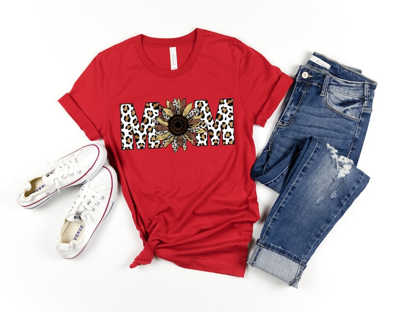 May include: Red short-sleeved t-shirt with a graphic of the word "MOM" in leopard print with a sunflower in the center.