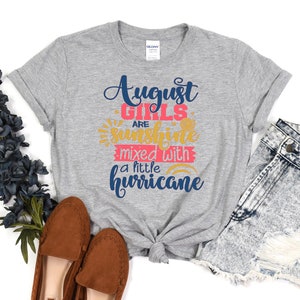 May include: Gray t-shirt with the text "August Girls are sunshine mixed with a little hurricane" in blue, pink, and yellow lettering.
