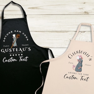 May include: Two black and beige kitchen aprons with a cartoon rat chef design. The text on the aprons reads "Anyone can cook" and "Gusteau's" with the words "Paris" and "France" on each apron. The text "Custom Text" is also on each apron.