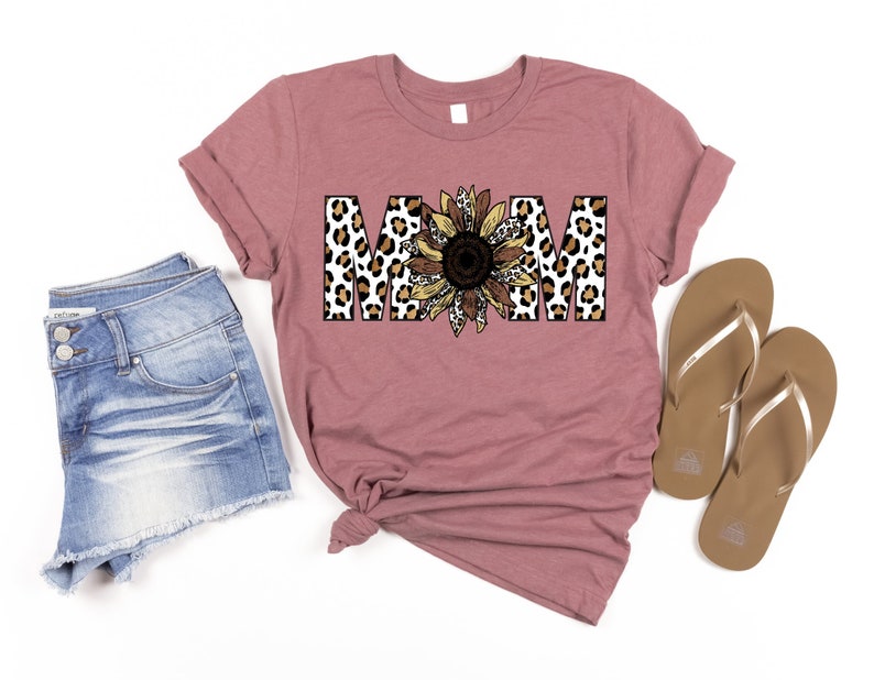 May include: A mauve t-shirt with the word "MOM" in brown, black, and white leopard print letters with a sunflower in the center.
