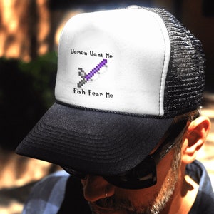 May include: A white and black trucker hat with a pixelated sword graphic and the text "Women Want Me Fish Fear Me".