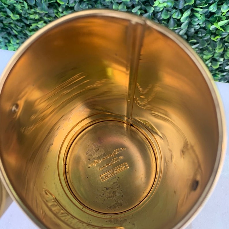 May include: Gold metal can with a smooth, shiny surface. The inside of the can is visible, showing a circular bottom with a label that reads "Dennison Mfg. Co.  Framingham, Mass."