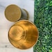 May include: Two gold metal containers with a crescent moon design. The top of one container reads "Telenora Not suitable for food Made in Holland".