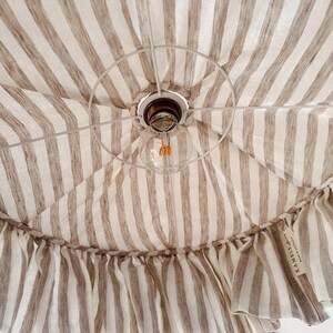 May include: A white and brown striped fabric canopy with a ruffled edge. The canopy has a light bulb hanging from it. The fabric has a label that says "RAMBLE" on it.