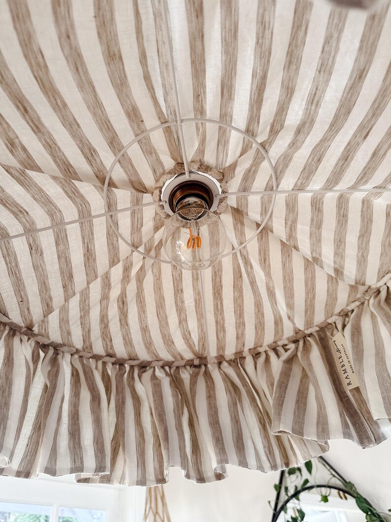 May include: A white and brown striped fabric canopy with a ruffled edge. The canopy has a light bulb hanging from it. The fabric has a label that says "RAMBLE" on it.