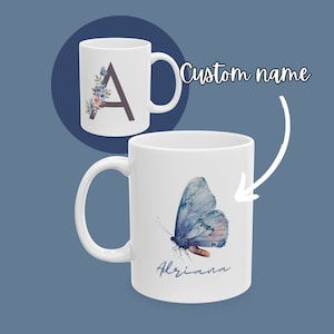 Puede incluir: Taza de cerámica blanca con un diseño de mariposa en acuarela en tonos azules y rosas, con el nombre "Adriana" en escritura cursiva. Otra taza muestra la letra "A" con detalles florales. Las palabras "Custom name" también son visibles.