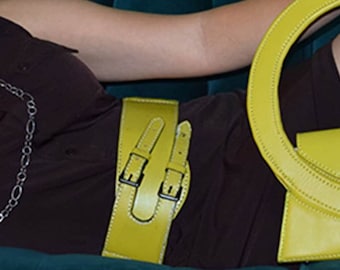 May include: A yellow leather belt with two buckles, worn over a dark brown top. The belt is wide and has a smooth, polished finish.