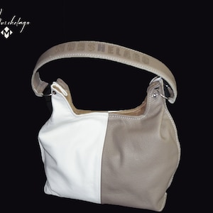 May include: A white and beige leather handbag with a brown leather strap. The strap has the word "Muishelango" embossed on it.