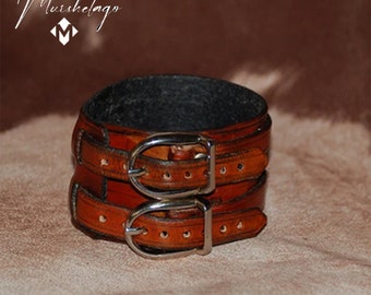 May include: A brown leather bracelet with two silver buckles. The bracelet is made of two layers of leather, and the buckles are double-pronged.