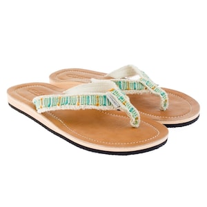 Può includere: Un paio di infradito in pelle marrone con cinturino in tela bianca e un design intrecciato verde e arancione.