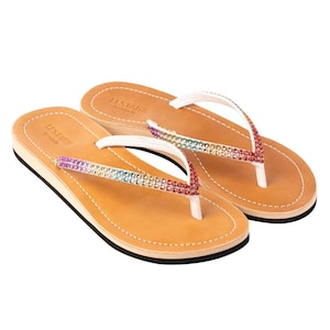 May include: A pair of brown leather thong sandals with a white strap and a rainbow-coloured rhinestone embellishment. The sandals are made by the brand "Les Tropiques".
